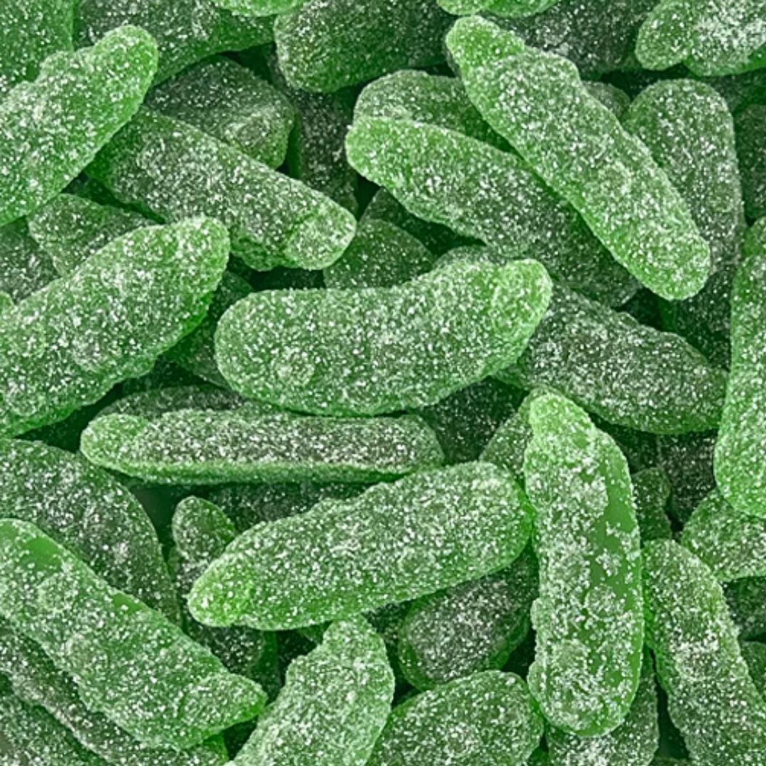 A close-up pile of bright green, sugar-coated gummy candies shaped like small elongated fruits or vegetables, filling the entire frame.