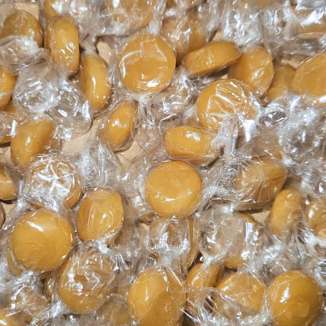 Individually wrapped butterscotch hard candies in a clear wrapper, showing the candy's shape and color.