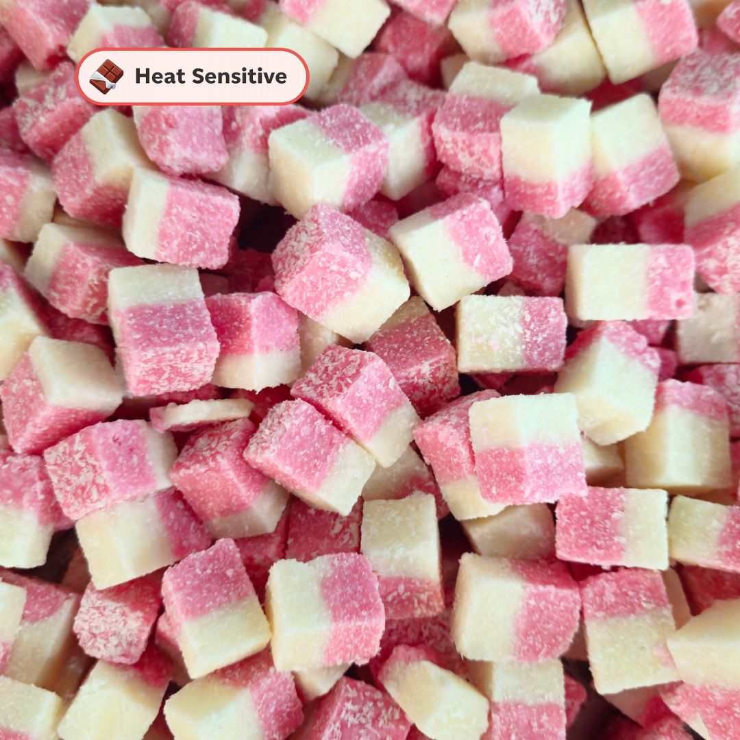 A close-up pile of small cubical candies or gummies, each showing two-tone pink and off-white halves coated with sugar. A small label in the upper left reads 'Heat Sensitive'.