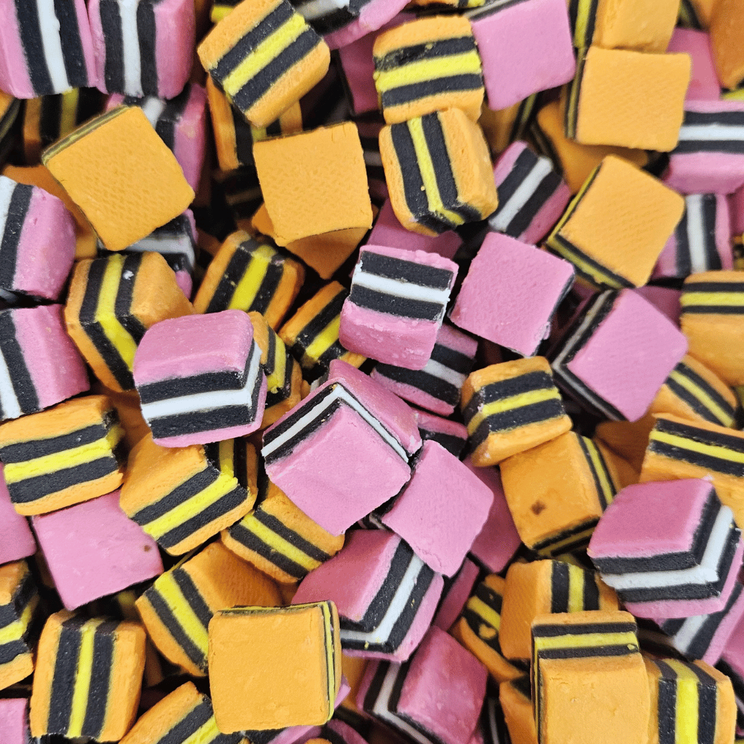 A collection of variously colored licorice allsorts pieces, including pink, yellow, black, and white, with a textured and chewy consistency.