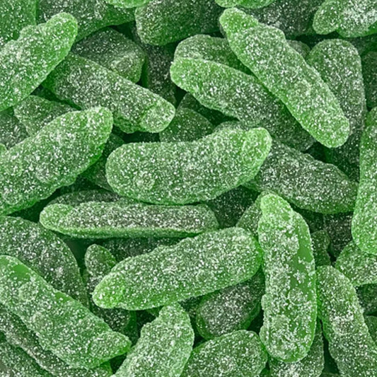 A close-up pile of bright green, sugar-coated gummy candies shaped like small elongated fruits or vegetables, filling the entire frame.