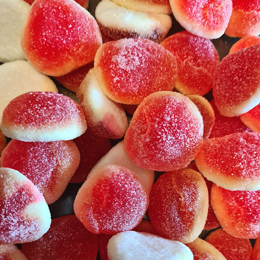A close-up of small, round, red and white candy pieces resembling damel-filled peaches.